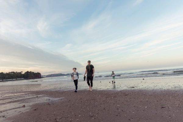 A family walking on a red-sand Torbay beach at dusk